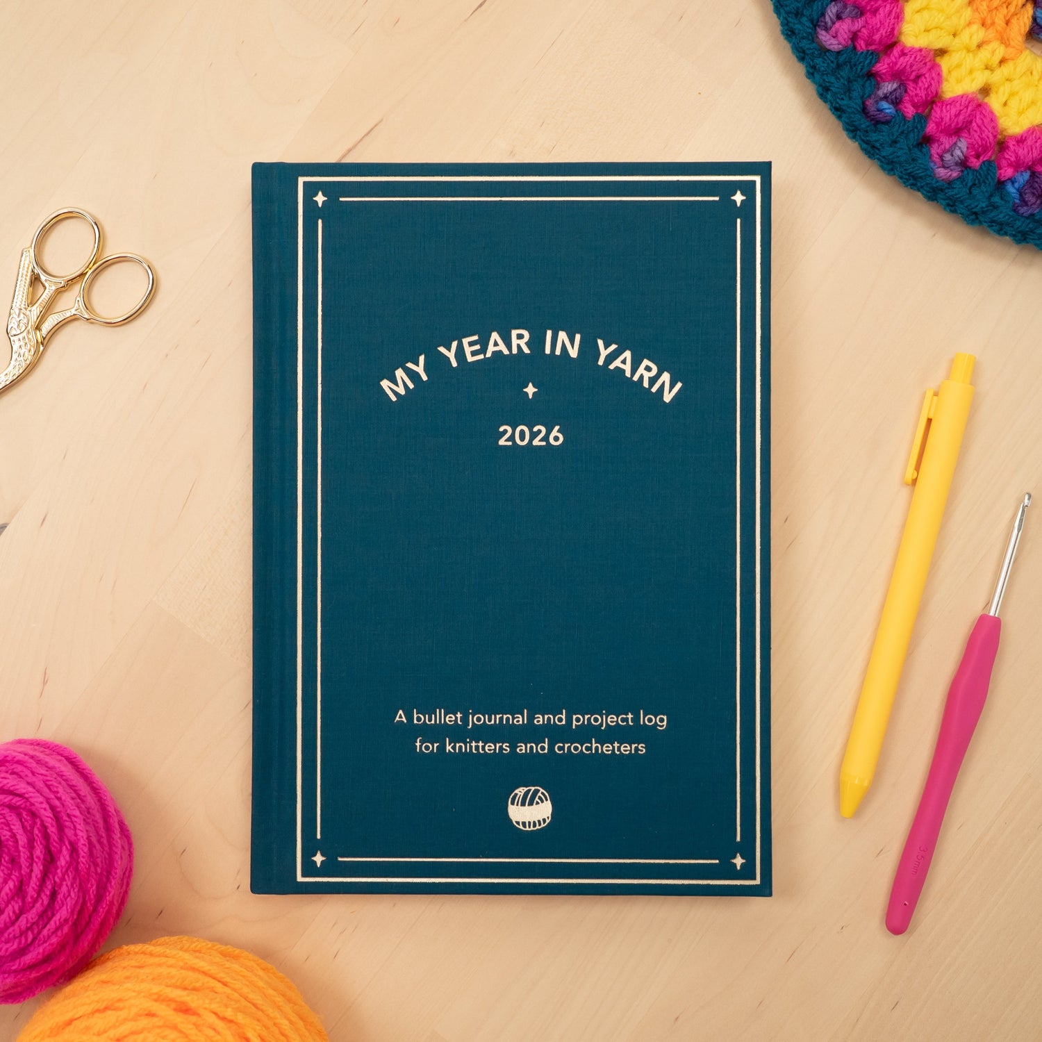 2026 planner for knitters and crocheters with yarn, scissors, and crochet hook on a wooden surface